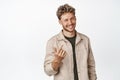 Handsome smiling man asking to come closer, luring you, looking friendly and beckon to approach him, standing over white Royalty Free Stock Photo