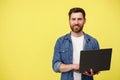 Handsome smiling man with beard holding laptop and looking at camera on yellow background Royalty Free Stock Photo