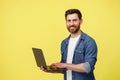 Handsome smiling man with beard holding laptop and looking at camera on yellow background Royalty Free Stock Photo