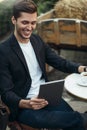 Handsome smiling man in casual wear checking email or reading world news on digital tablet computer drinking morning coffee, Royalty Free Stock Photo