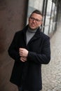 Handsome smiling man in glasses and black coat near building. Portrait of business man walking outdoors in cold day. Royalty Free Stock Photo