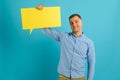 Handsome smiling man holding blank speech bubble sign isolated on light blue studio banner background with copy space Royalty Free Stock Photo