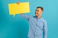 Handsome smiling man holding blank speech bubble sign isolated on light blue studio banner background with copy space Royalty Free Stock Photo