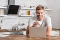 handsome smiling man holding cup of coffee and looking at laptop Royalty Free Stock Photo