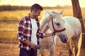 Handsome smiling man leading his white horse . Fun on countryside, sunset golden hour. Freedom nature concept Royalty Free Stock Photo