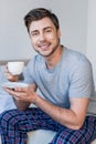 Handsome smiling man in pyjamas holding coffee cup and looking at camera. Royalty Free Stock Photo