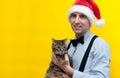 Man in red santa hat, blue shirt and black suspender holding cute brown tabby cat and looking at camera Royalty Free Stock Photo