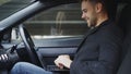 Attractive smiling man typing laptop computer while sitting inside his car outdoors Royalty Free Stock Photo