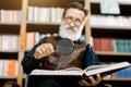 Handsome smiling senior bearded man, librarian or professor, in the library, sitting on the background of bookcases Royalty Free Stock Photo