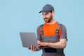 Handsome smiling worker man in uniform work on laptop on blue studio background Royalty Free Stock Photo