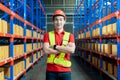 Handsome Smiling Worker Wearing Hard Hat, Standing with Crossed Arms in the Retail Warehouse full of Shelves Royalty Free Stock Photo