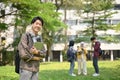 Smiling Asian male college student carrying his laptop and backpack and standing in the park Royalty Free Stock Photo