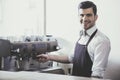 Handsome smiling young barista doing coffee in coffeehouse.