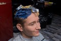 Handsome smiling young guy portrait European in the process of dyeing hair in color in a barbershop
