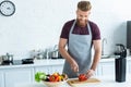 handsome smiling young man in apron cutting bell pepper on wooden Royalty Free Stock Photo