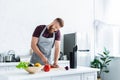 handsome smiling young man in apron talking by smartphone and cooking in kitchen Royalty Free Stock Photo