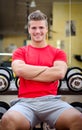 Handsome smiling young man in gym sitting on dumbbells rack Royalty Free Stock Photo