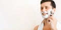 Handsome smiling young man with towel on his shoulders shaves with modern straight razor indoors, banner with copy space Royalty Free Stock Photo