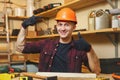 Handsome smiling young man working in carpentry workshop at wooden table place with piece of wood