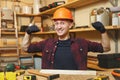 Handsome smiling young man working in carpentry workshop at wooden table place with piece of wood