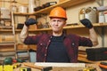 Handsome smiling young man working in carpentry workshop at wooden table place with piece of wood