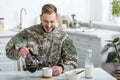 Handsome soldier in uniform smiling and pouring coffee in cup