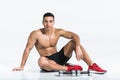 Sportive mixed race man sitting on floor near dumbbells on white