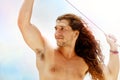 A handsome sporty guy with long hair against a blue clear sky with white clouds. Light background. Royalty Free Stock Photo