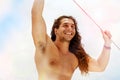 A handsome sporty guy with long hair smiling against a blue clear sky with white clouds. Journey on a yacht by sea.