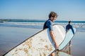 Handsome sporty young surfer posing with his surfboard under his arm in his wetsuit on a sandy tropical beach Royalty Free Stock Photo