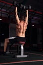 Handsome strong brutal man sitting on the bench doing the exercises with dumbbells on dark sport club background. Training