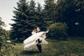 Handsome strong groom holding happy bride in the air, newlywed couple posing in summer park, groom carrying beautiful bride, Royalty Free Stock Photo