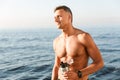 Handsome strong mature sportsman drinking on the beach.