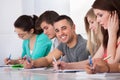 Handsome student sitting with classmates writing at desk Royalty Free Stock Photo