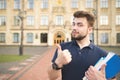 Handsome student standing with books in the hands of the university building background and showing a thumbs up Royalty Free Stock Photo