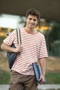 Handsome student wearing a bacpack and holding a folder looking at camera.Relaxed and happy young man standing outside Royalty Free Stock Photo