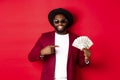Handsome and stylish african american male model showing money and smiling, wearing sunglasses and fancy hat, standing