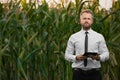 Handsome, stylish, blonde, businessman holding a black, new tablet and standing in the middle of green and yellow corn field Royalty Free Stock Photo