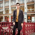 Handsome stylish fashionable man, brunette in elegant gray coat, stands on street in historical center of St. Petersburg. Young Royalty Free Stock Photo