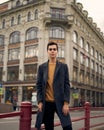 Handsome stylish fashionable man, brunette in elegant gray coat, stands on street in historical center of St. Petersburg. Young Royalty Free Stock Photo