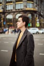 Handsome stylish fashionable man, brunette in elegant gray coat, stands on street in historical center of St. Petersburg. Young Royalty Free Stock Photo