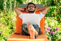 Handsome stylish indian man summer vacation in tropical paradise relaxing on an orange deckchair against a background of Royalty Free Stock Photo