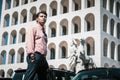 Handsome stylish man outdoors, with striped shirt. Sunglasses not worn. Building and cars in the background