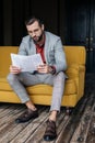 handsome stylish man in trendy suit reading newspaper and sitting