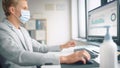 Handsome Stylish Young Man Wearing Protective Face Mask and Working at His Desk on Computer in Off Royalty Free Stock Photo