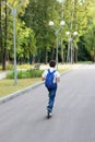 A handsome stylish and young schoolboy in a white shirt, blue tie and a backpack with a scooter on a street. back view Royalty Free Stock Photo