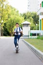 A handsome stylish and young schoolboy in a white shirt, blue tie and a backpack with a scooter on a street Royalty Free Stock Photo