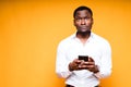 Handsome surprised african american man holding phone while standing on yellow background