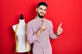 Handsome tailor man with beard standing by manikin smiling and looking at the camera pointing with two hands and fingers to the