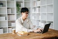 Handsome and talented young Asian man student working on his project assignment, using laptop and tablet to search an online Royalty Free Stock Photo